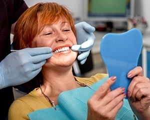 Senior woman in dental chair examining smile in mirror