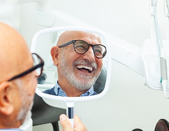 A man smiling at his dental implants in the mirror.
