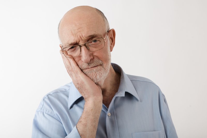 Older man holding his cheek because of ill-fitting dentures
