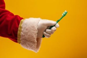 Santa's arm holding a toothbrush in front of a yellow background