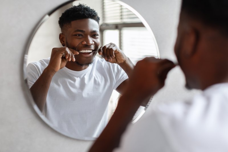 Patient smiling as they floss in the mirror